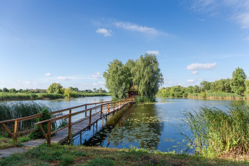 Fototapeta na wymiar Small footbridge to island with hut and trees on lake