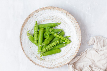 Fresh green peas in rustic plate on white marble background with copy space