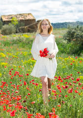 Woman  in white dress walking and holding bouquet of poppies plants