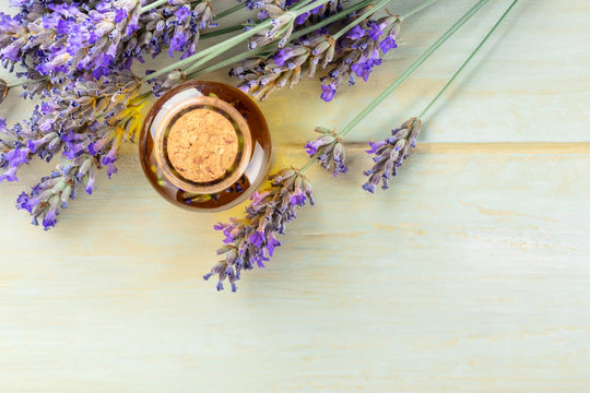 Lavender essential oil with lavender flowers on a rustic wooden background with a place for text. A glass bottle, shot from the top with a cork with buds infusing