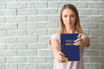 Religious young woman with Bible against brick wall