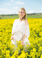 Naklejka na ściany i meble Young woman in yellow oilseed rape field posing in white dress