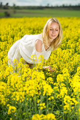 Fototapeta premium Girl posing in rape seed flowers field posing in white dress at sunny day