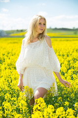 Fototapeta premium Young female posing in yellow oilseed rape field wearing in white dress