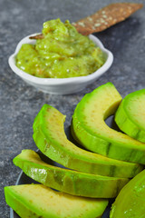 Guacamole in a bowl on a background of sliced avocado.