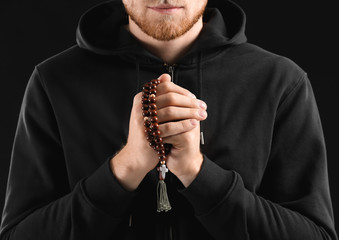 Fototapeta na wymiar Religious young man praying to God on dark background, closeup