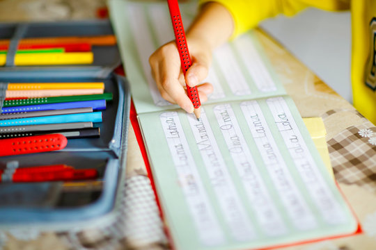 lose-up of little kid boy at home making homework, child writing first letters and words like mama with colorful pens. Elementary school and education