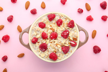 Bowl with tasty sweet oatmeal, almond and raspberry on color background
