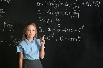 Little schoolgirl with raised index finger near blackboard