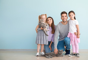 Happy family with cute cats near light wall