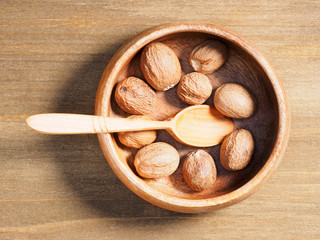 Spice Nutmeg (Myristica fragrans) in a wooden cup on a wooden background with spoon