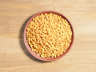 Spice Fenugreek (Trigonetla) on a brown clay plate on a wooden background
