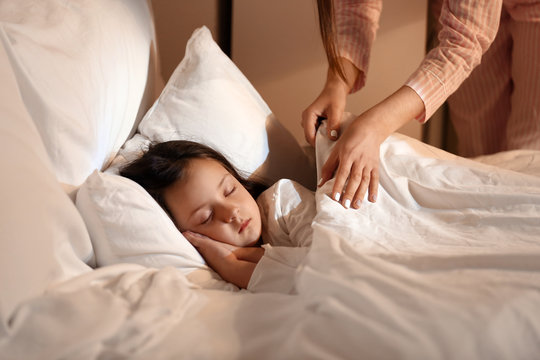 Woman putting her little daughter to bed