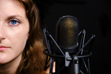 Professional record of the singer, close-up. Female vocalist on black background in recording Studio. Brunette girl for a silver microphone.