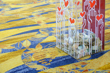 Transparent donation box filled with some banknotes on carpet floor