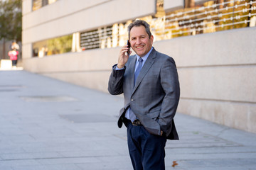 Portrait of handsome middle aged smart businessman walking in the city talking on mobile phone