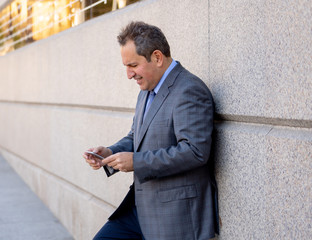 Middle aged handsome businessman using mobile phone app sending message outside office in urban city