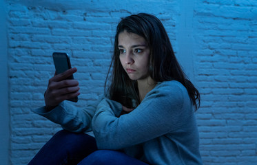 Young sad woman alone looking at smart phone in fear suffering Internet harassment and cyberbullying