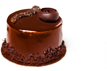 A delicious chocolate cake with chocolate pieces lies on a wooden stand next to a white cup, which stands on a white table