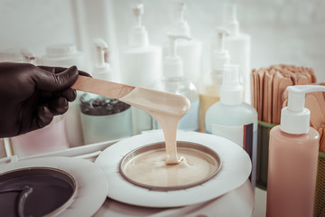 Beauty salon worker taking melted wax with wooden spatula