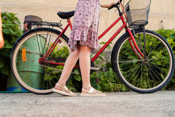 Naklejka premium Close up on woman's legs female standing beside the bicycle wearing summer dress in a sunny day