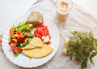 Healthy breakfast. Omelette with tomatoes and rucola salad. Salmon with wholemeal bread. Cappuccino and roses on the rustic linen background. Ideal morning flat lay.