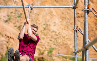 Fit man overcome obstacles using rope during extreme race in the boot camp
