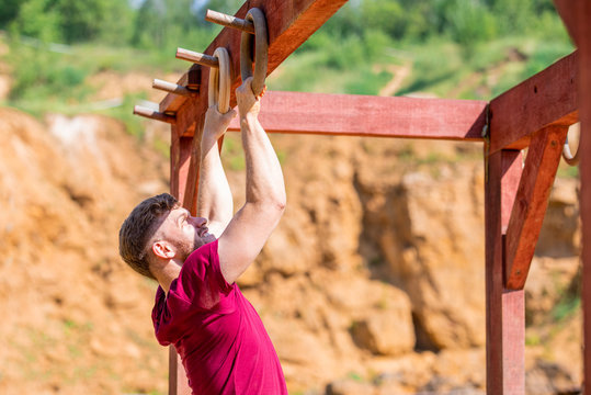 Fit man overcome obstacles using rings during extreme race in the boot camp - Powered by Adobe