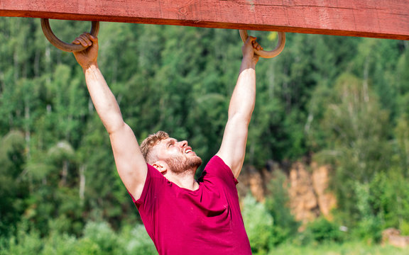 Fit man overcome obstacles using rings during extreme race in the boot camp - Powered by Adobe