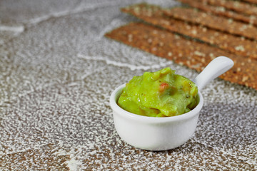 Guacamole in presentation bowl with crispy rye chips on light surface.