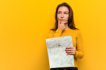 Young european woman holding a map looking sideways with doubtful and skeptical expression.