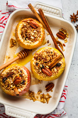 Baked apples with granola, cranberries, nuts and honey in oven dish.