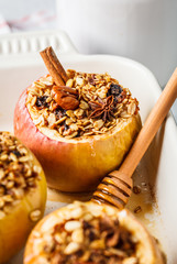 Baked apples with granola, cranberries, nuts and honey in oven dish.