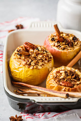 Baked apples with granola, cranberries, nuts and honey in oven dish.