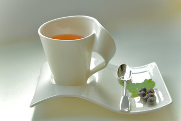 stylish cup with tea with a leaf and fruits of currants with a silver spoon
