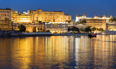 Fototapeta na wymiar Historic Udaipur City palace illuminated at Blue hour. Beautiful reflections on Lake Pichola. Long exposure Shot from Ambrai Ghat. Post sunset view with Boat rides 