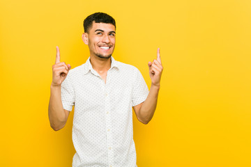 Young hispanic man indicates with both fore fingers up showing a blank space.