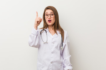 Young doctor woman against a white wall having an idea, inspiration concept.