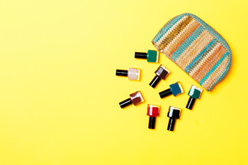 Woman cosmetic bag with manicure and pedicure, bright gel varnishes on yellow background with copy space for your design and text. Nail work flat lay concept
