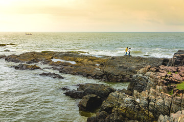 Gokarna, Karnataka India - October 10 2016: An unidentified couple take  a walk on the rocky cliff of Om beach in Gokarna, Karnataka, India at sunset. Aum/Om shaped beach . Boat passing at Horizon