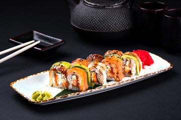 Close up rainbow Sushi Roll with salmon, eel, tuna, avocado, royal prawn, cream cheese Philadelphia, caviar tobica, chuka. Sushi menu. Japanese food and green tea teapot, copyspace.