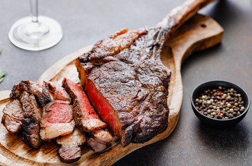 Grilled dry-aged marble beef steak Tomahawk on black wooden board with spices.