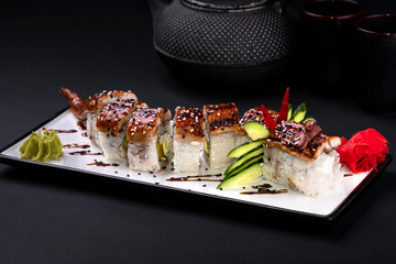 Top view close up of sushi roll Red Dragon and soy on black background. Traditional china Golden dragon rolls with tuna, eel, cucumber, sesame seeds and tobiko caviar. Green teapot