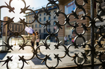 Fototapeta na wymiar View through metal fence on city in the morning sun backlight.