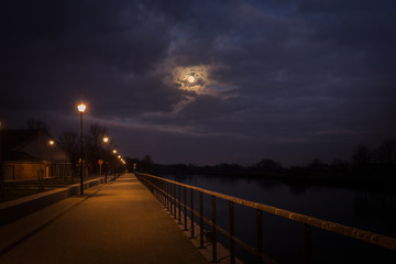 the full moon comes squeaking among the dramatic clouds on the Leie in Wervik, Belgium