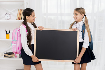 Cheerful schoolgirls with backpacks holding blackboard in room