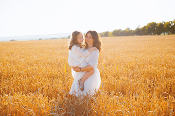 Photo of a handsome mother holding his daughter and posing in a wheat field