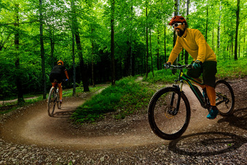 Cycling woman and men riding on bikes at sunset mountains forest landscape. Couple cycling MTB enduro flow trail track. Outdoor sport activity.