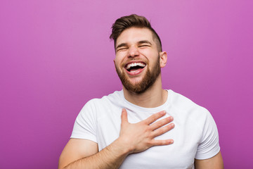 Young handsome caucasian man laughs out loudly keeping hand on chest.
