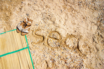 sandals and a rug lie on a shell beach